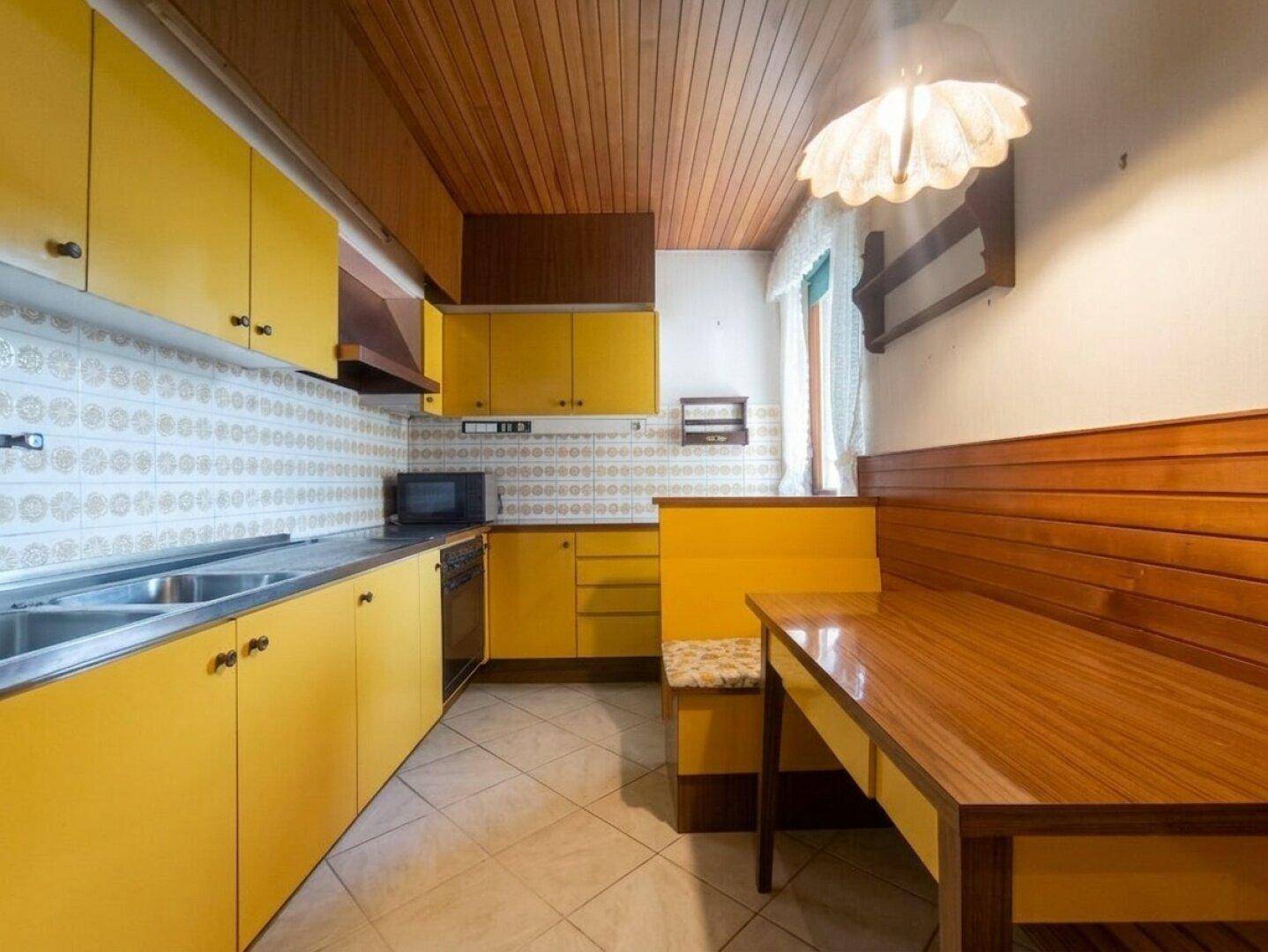Traditionelle Küche mit gelben Schränken, Holztäfelung an der Decke und gemütlicher Essecke.