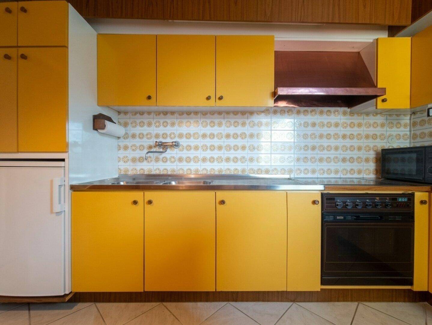 Detailansicht der Küche mit gelben Unterschränken, Spüle, Backofen und Mikrowelle.