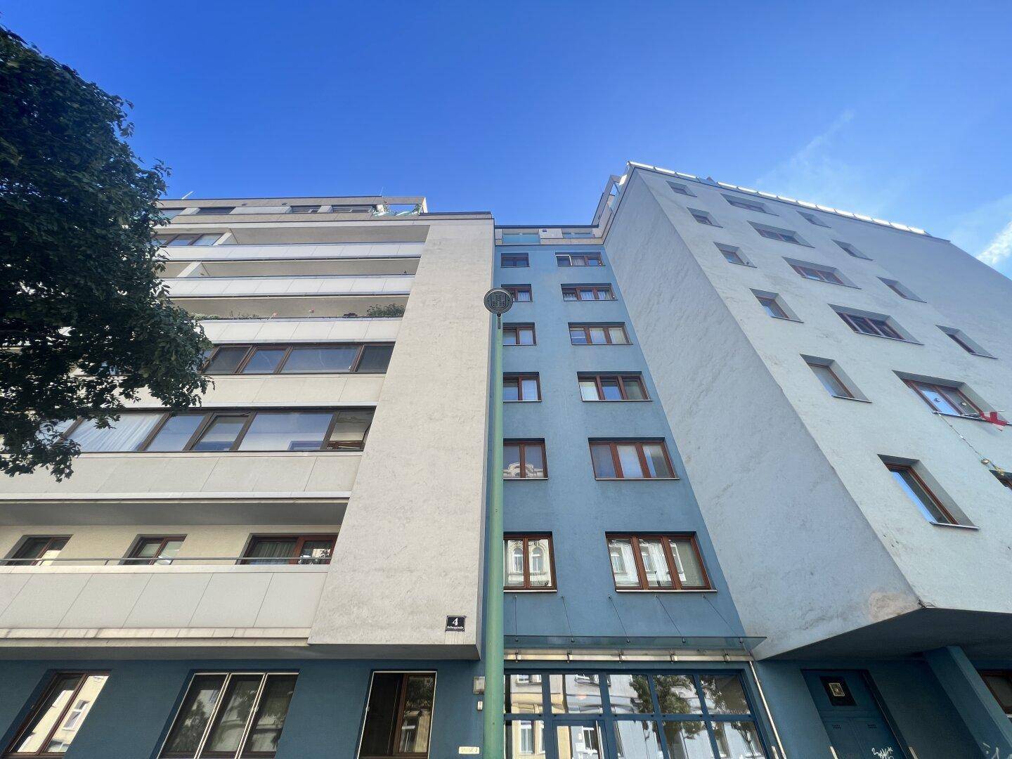 Mehrstöckiges Wohngebäude mit blauer Fassade und Balkonen unter klarem blauem Himmel.