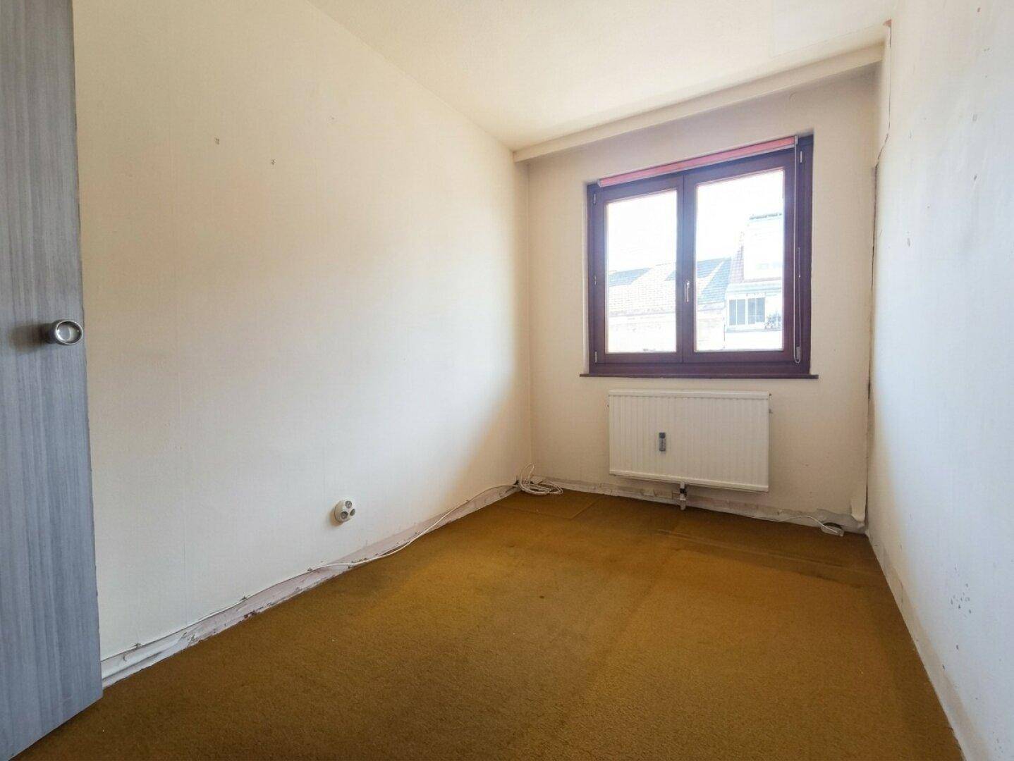 Unmöbliertes Schlafzimmer mit altem gelbem Teppichboden und Fenster, das eine Modernisierung benötigt.
