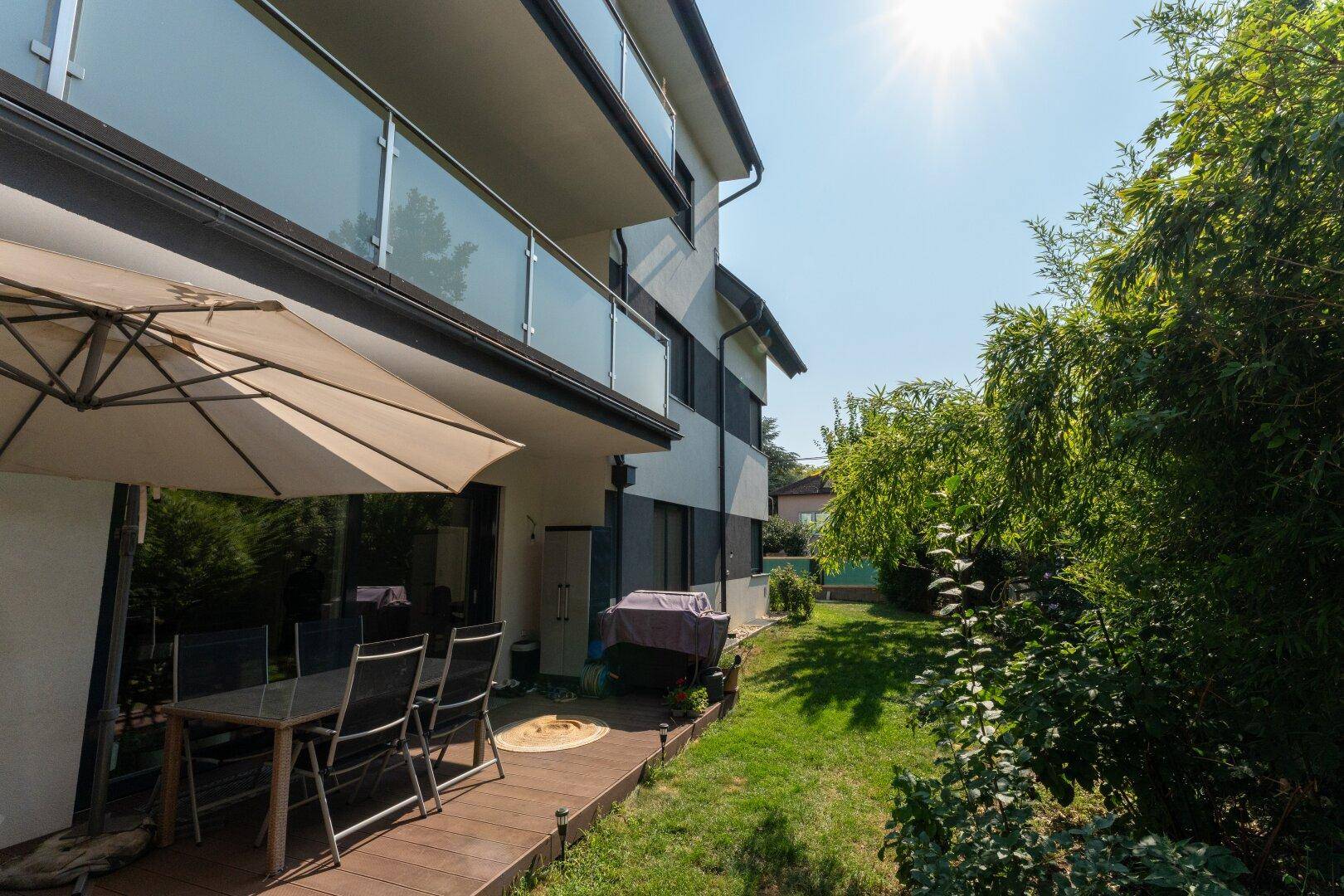 Gemütliche Terrasse mit Holzboden, Sonnenschirm und Grillbereich, angrenzend an einen grünen Garten.