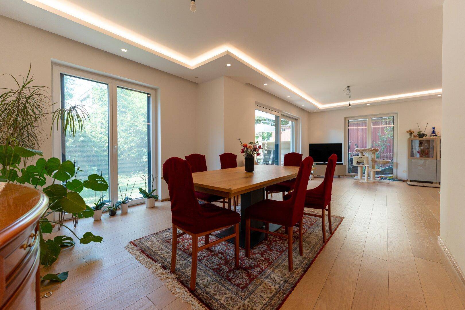 Heller Essbereich mit Holztisch, roten Stühlen und Zugang zum Garten durch große Fenster.