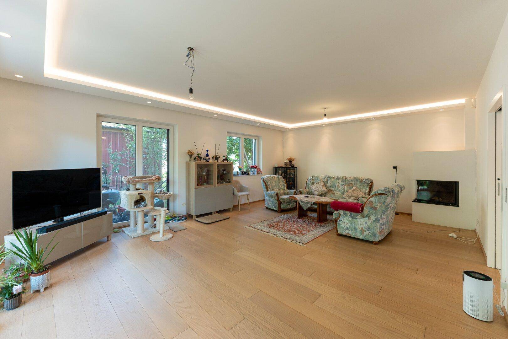 Gemütliches Wohnzimmer mit Holzboden, Kamin und indirekter Deckenbeleuchtung.