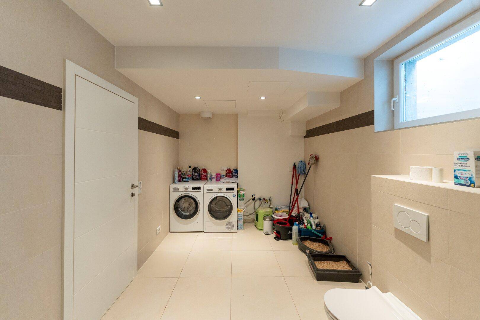 Praktischer Hauswirtschaftsraum mit Waschmaschine, Trockner und einer Toilette.