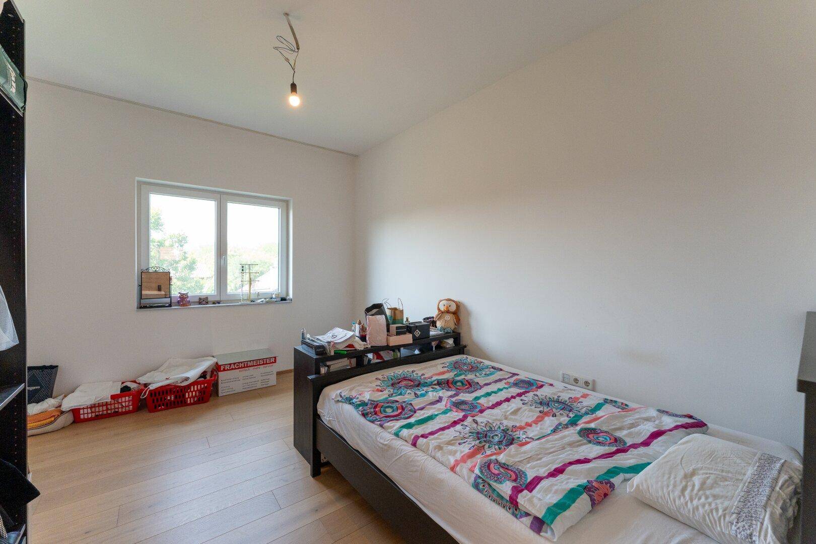 Helles Schlafzimmer mit Holzboden, weiß gestrichenen Wänden und einem großen Fenster.