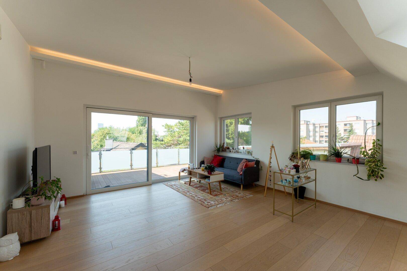 Helles Wohnzimmer im Dachgeschoss mit Holzboden, Zugang zur Terrasse und indirekter Beleuchtung.