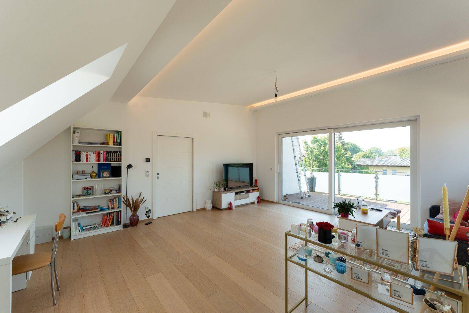 Geräumiges Dachgeschoss-Wohnzimmer mit Holzboden, Bücherregal und Zugang zur Dachterrasse.