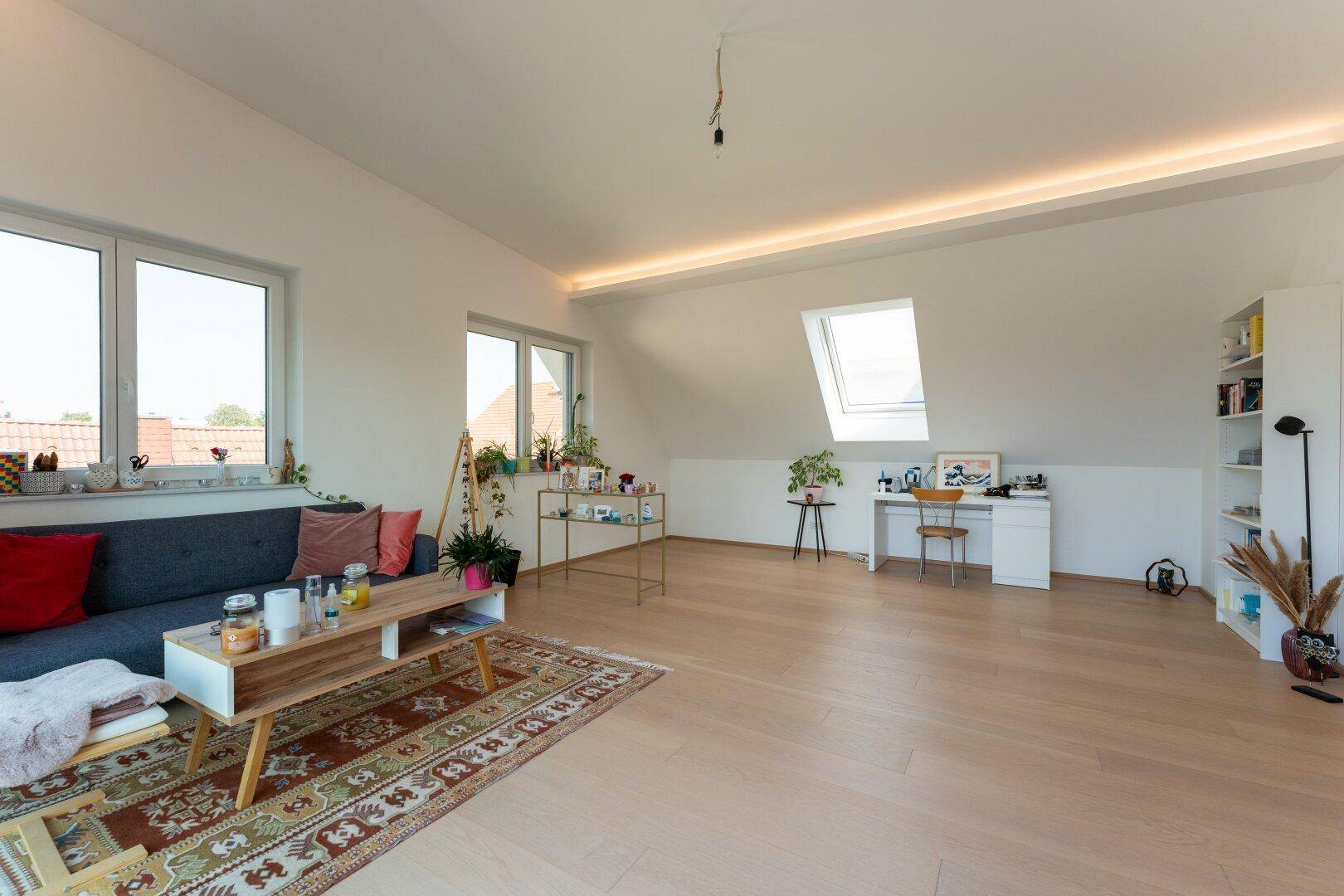Gemütliches Dachgeschoss-Wohnzimmer mit Holzboden, Sofa und Dachfenster für zusätzliches Licht.