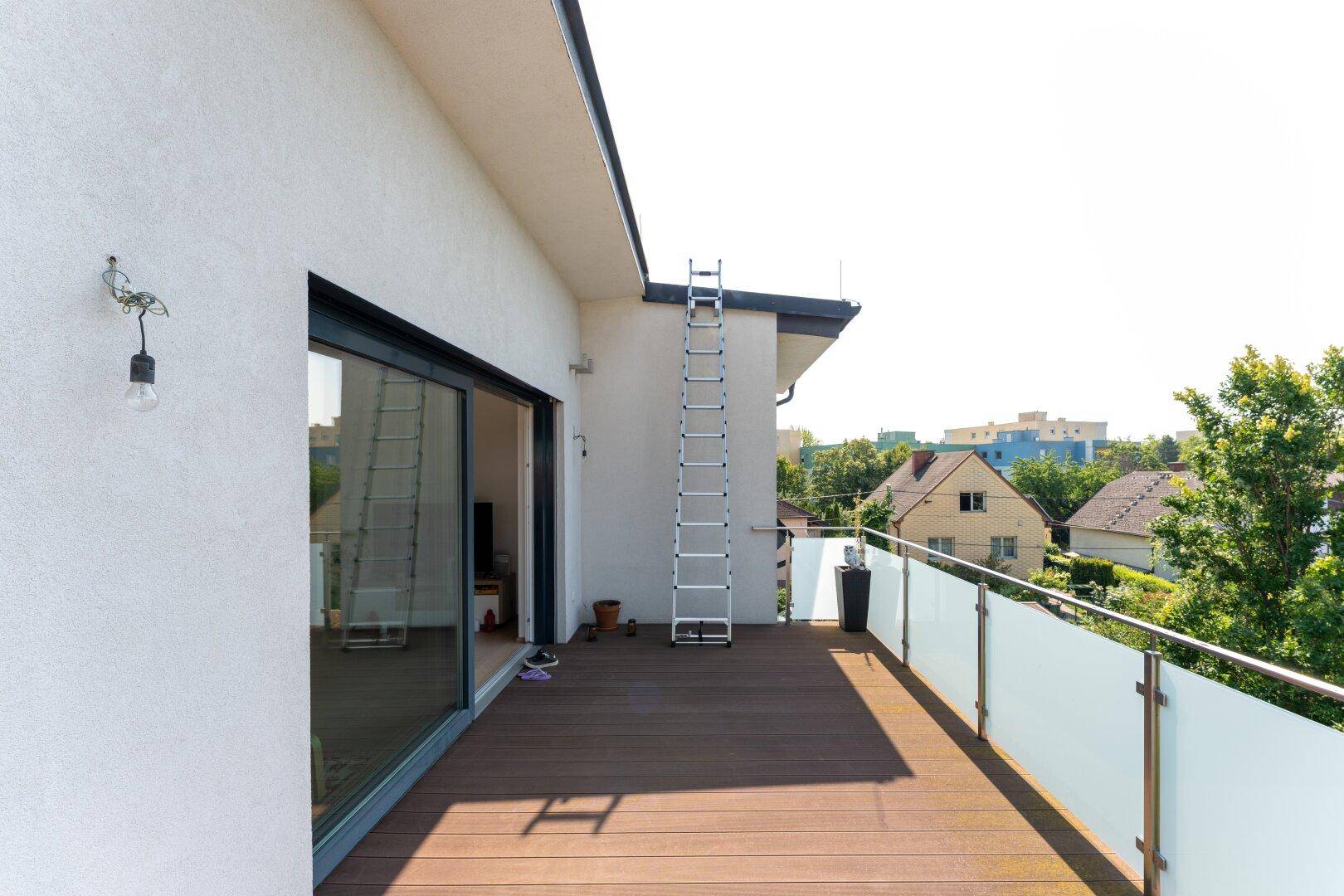 Geräumige Dachterrasse mit Holzboden, Glasgeländer und Blick auf die umliegenden Häuser.