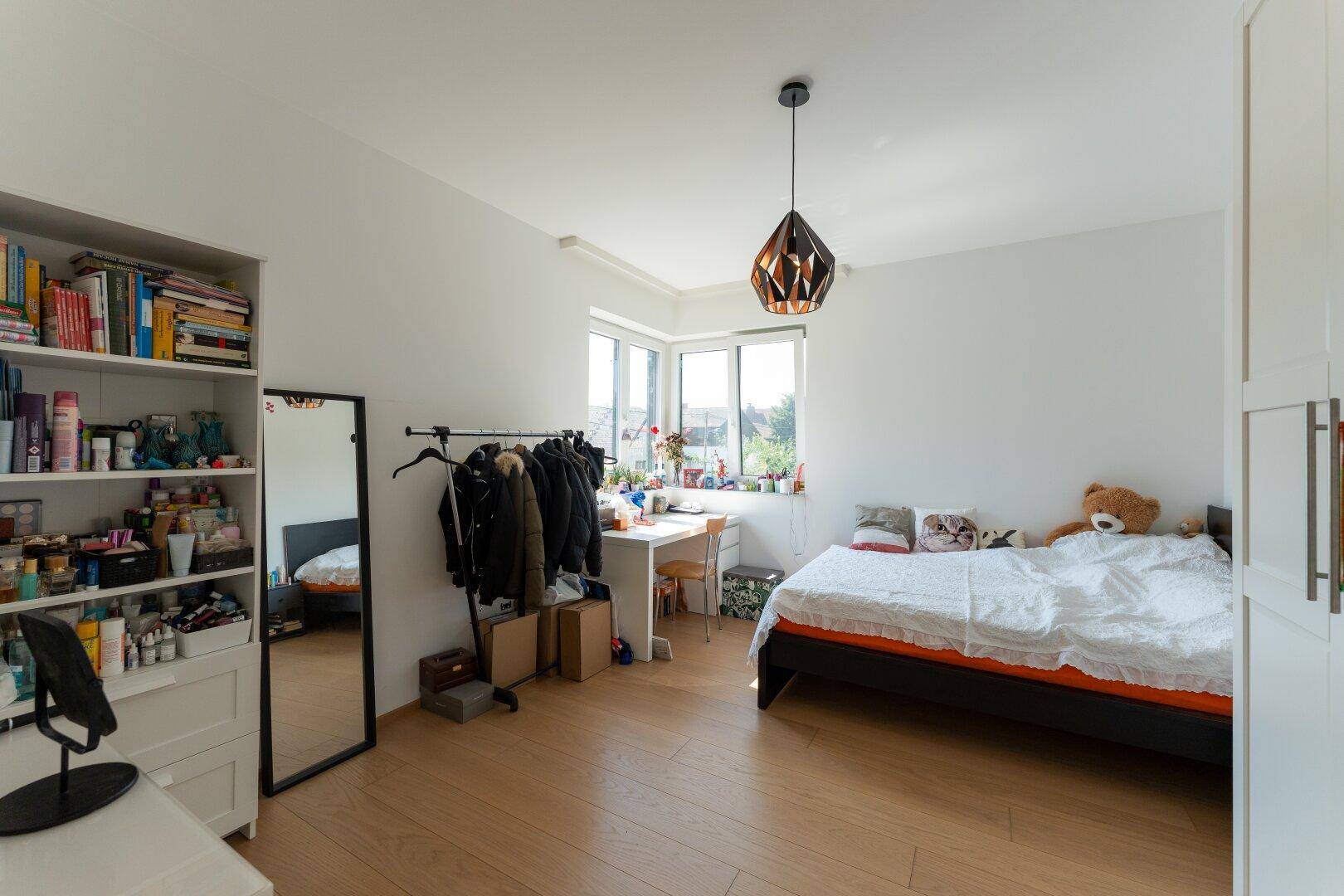 Helles Schlafzimmer mit Holzboden, großem Fenster und modernem Deckenlicht.