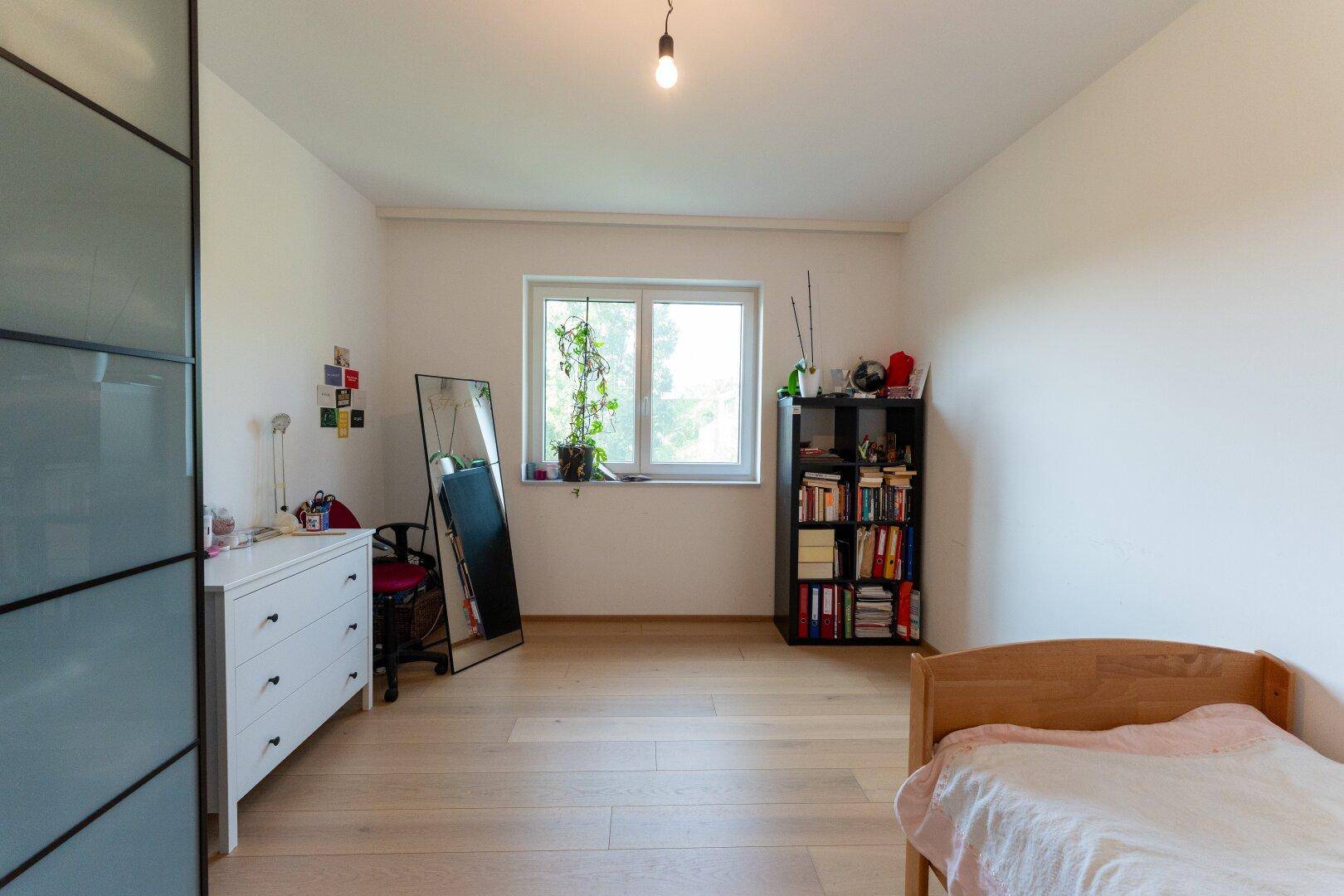 Einfaches Schlafzimmer mit Holzboden, weiß gestrichenen Wänden und einem großen Spiegel.