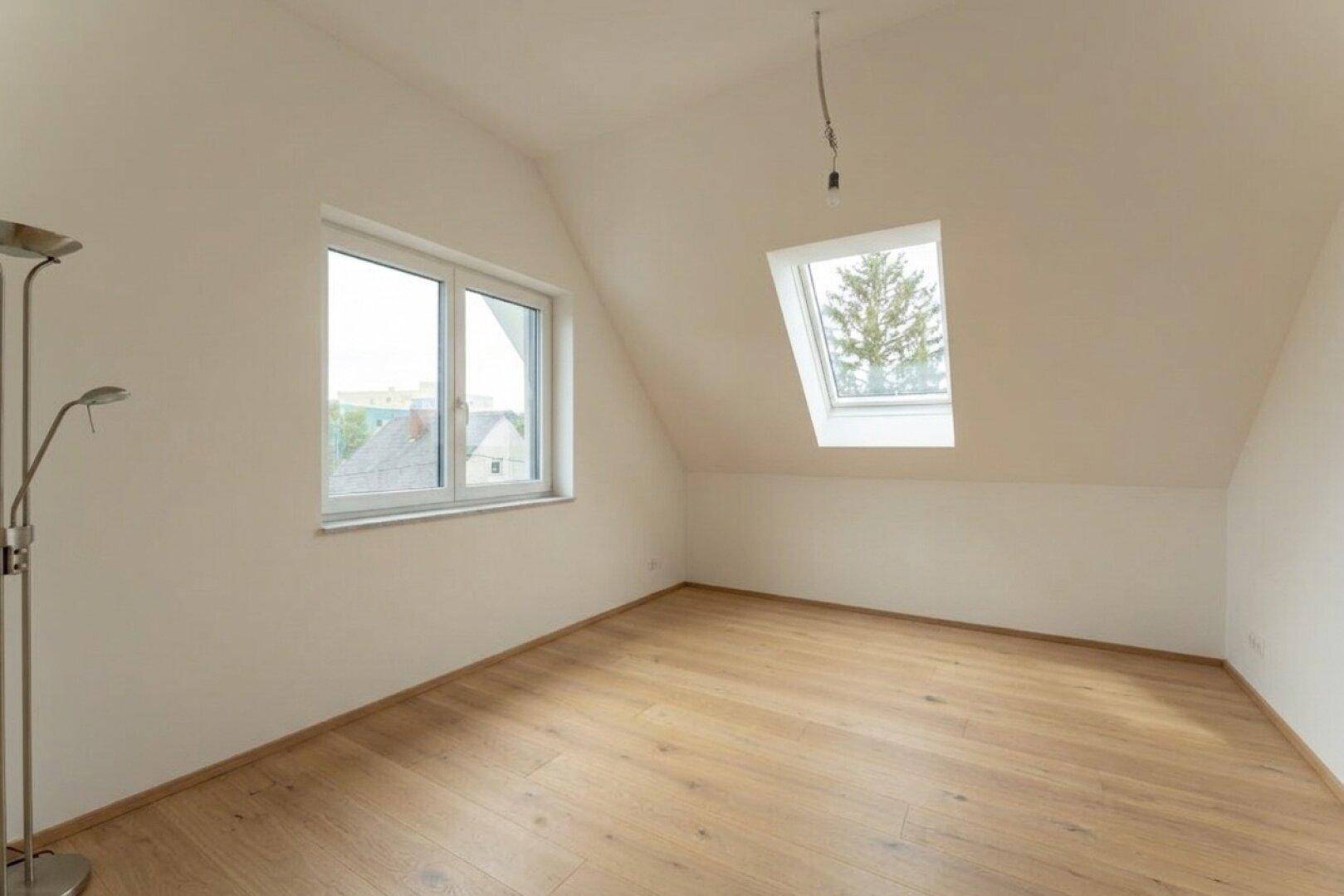 Helles Dachzimmer mit Holzboden, Dachschräge und einem Dachfenster für viel Licht.