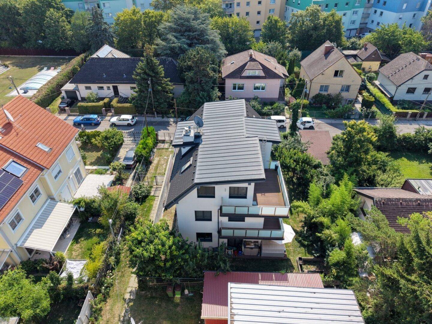 Luftaufnahme eines modernen Mehrfamilienhauses mit Satteldach und Balkonen, umgeben von viel Grün.
