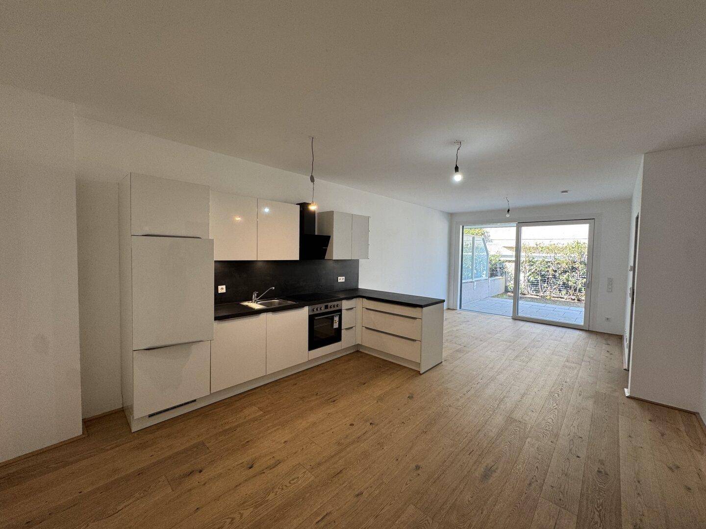Heller offener Wohnbereich mit moderner weißer Küche, Holzboden und Zugang zur Terrasse.