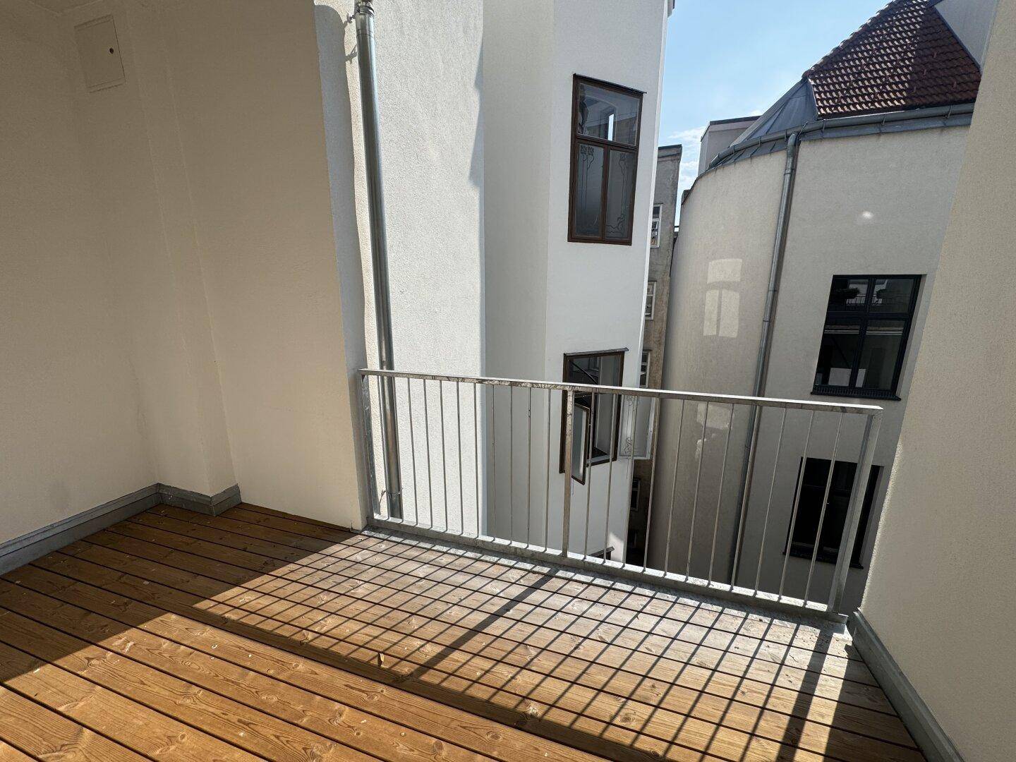 Sonniger Balkon mit Holzboden und Metallgeländer, bietet einen Blick auf die umliegenden Gebäude.