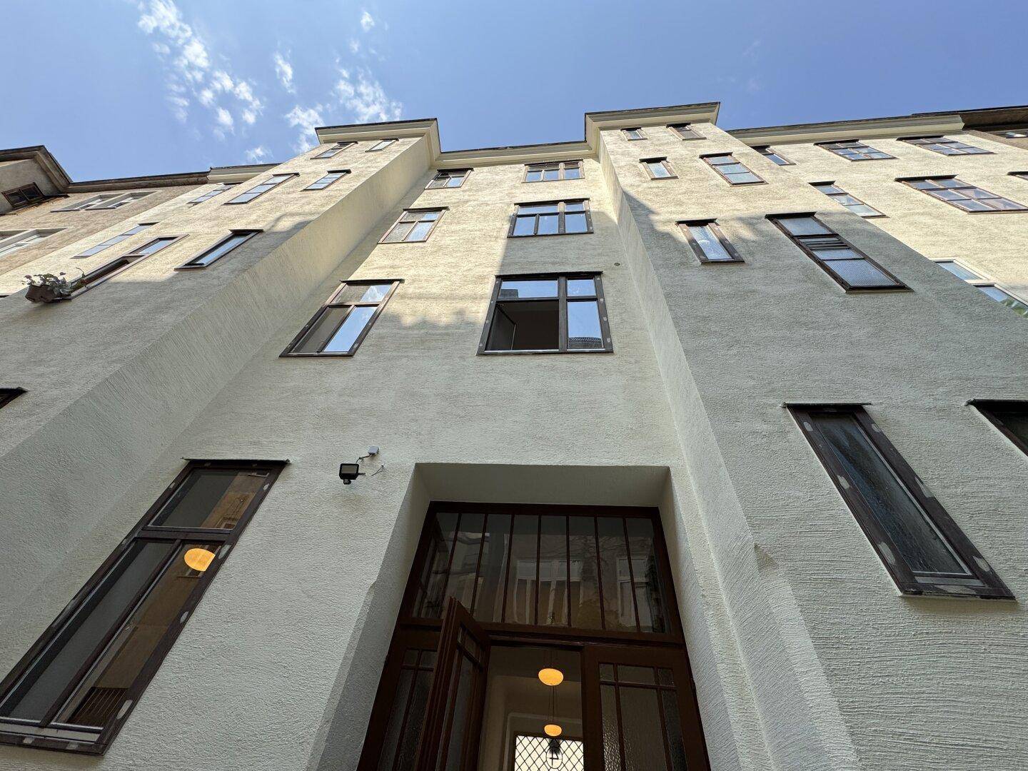 Fassade eines Wohngebäudes mit offener Eingangstür, Fenstern und einer Überwachungskamera.