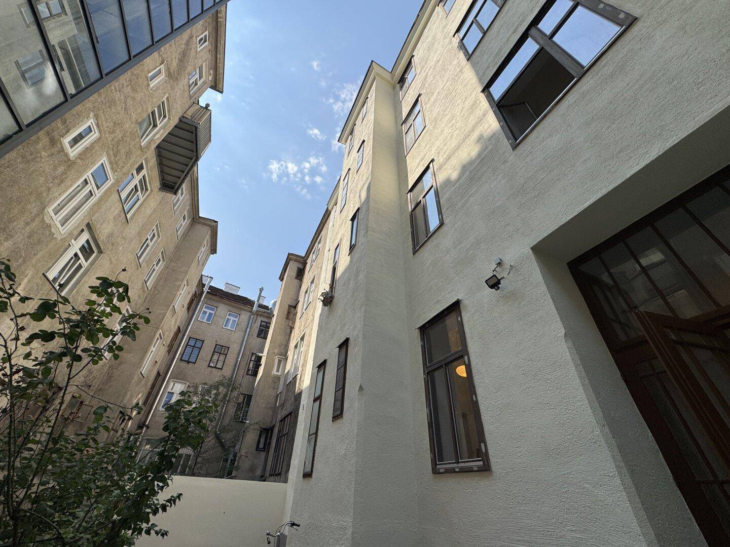 Blick in einen Innenhof mit hohen Gebäudefassaden und vielen Fenstern unter blauem Himmel.