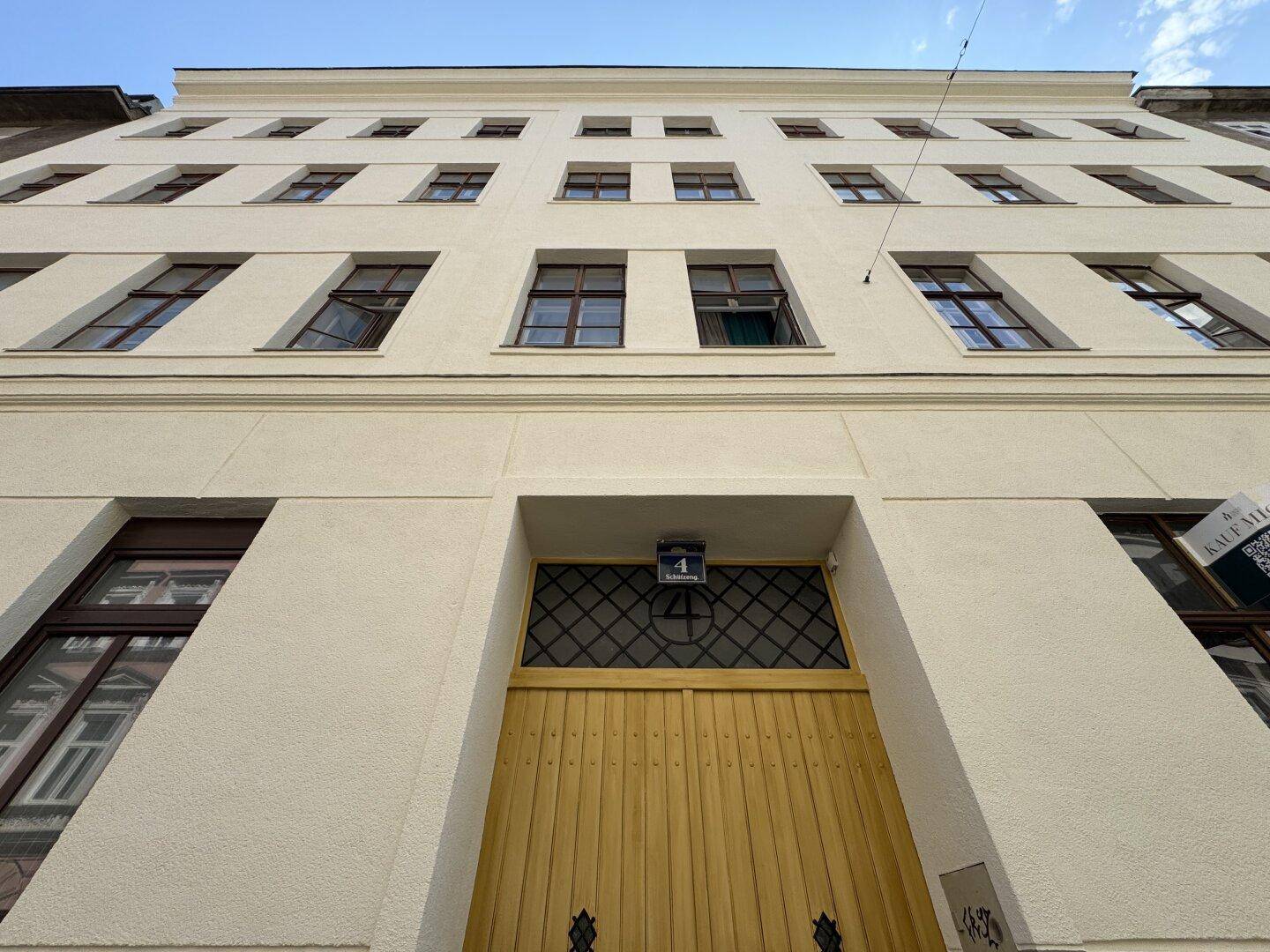 Historische Gebäudefassade mit vielen Fenstern und einem markanten gelben Eingangstor.