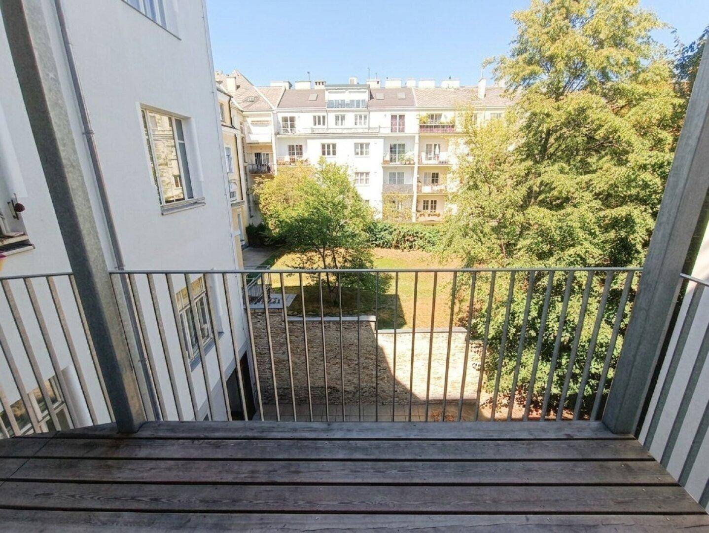 Heller Balkon mit Holzboden und weitem Blick auf den begrünten Innenhof und die Nachbargebäude.