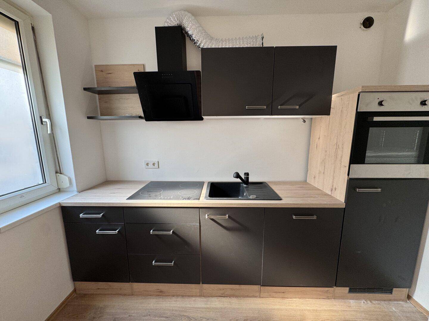 Moderne Einbauküche mit dunklen Fronten, heller Holzoptik-Arbeitsplatte und integrierten Geräten.