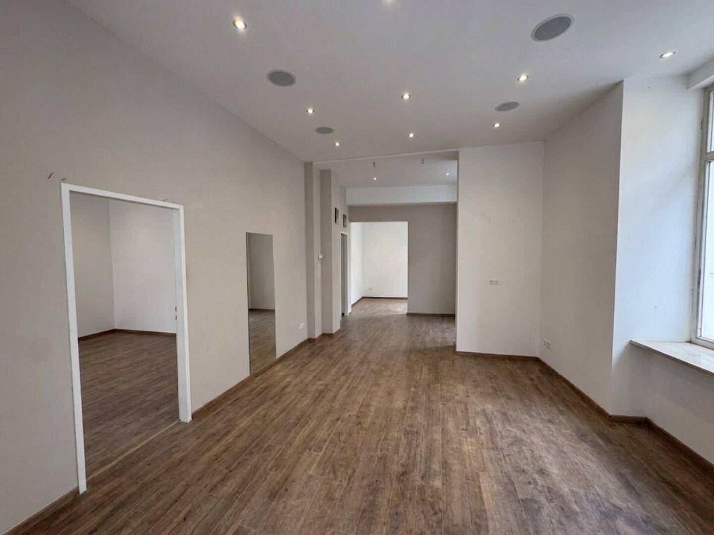 Großer, offener Raum mit Holzoptik-Boden, weißen Wänden und vielen Einbaustrahlern in der Decke.