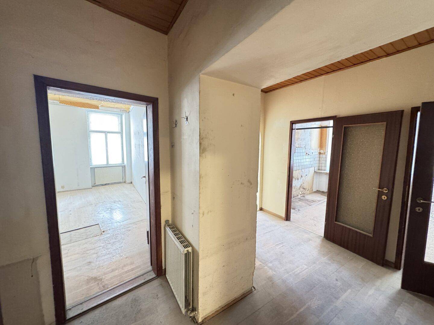 Flur mit Holztüren und sichtbaren Wänden, der zu verschiedenen Räumen führt, in renovierungsbedürftigem Zustand.