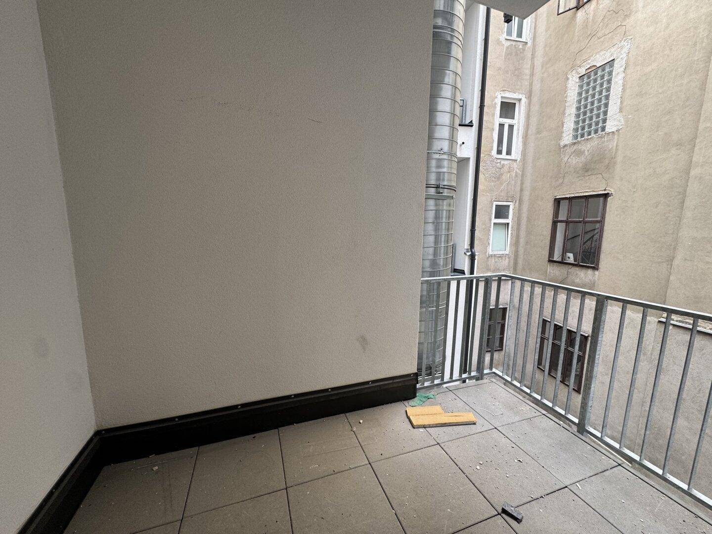 Kleiner Balkon mit Fliesenboden und Metallgeländer, umgeben von Gebäuden.