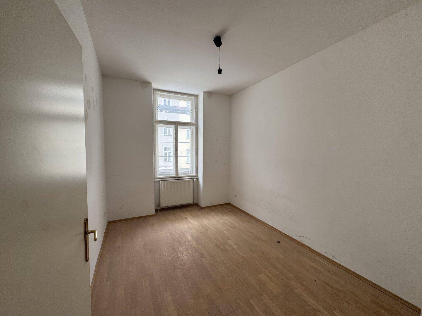 Heller, leerer Raum mit Holzboden und einem Fenster.