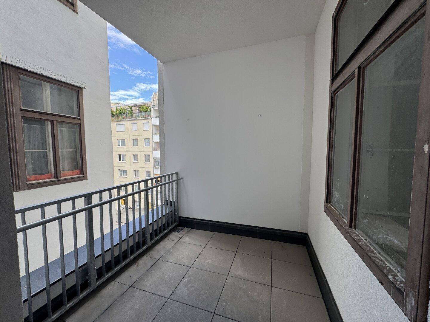 Kleiner Balkon mit Fliesenboden und Blick auf die umliegenden Gebäude der Stadt.