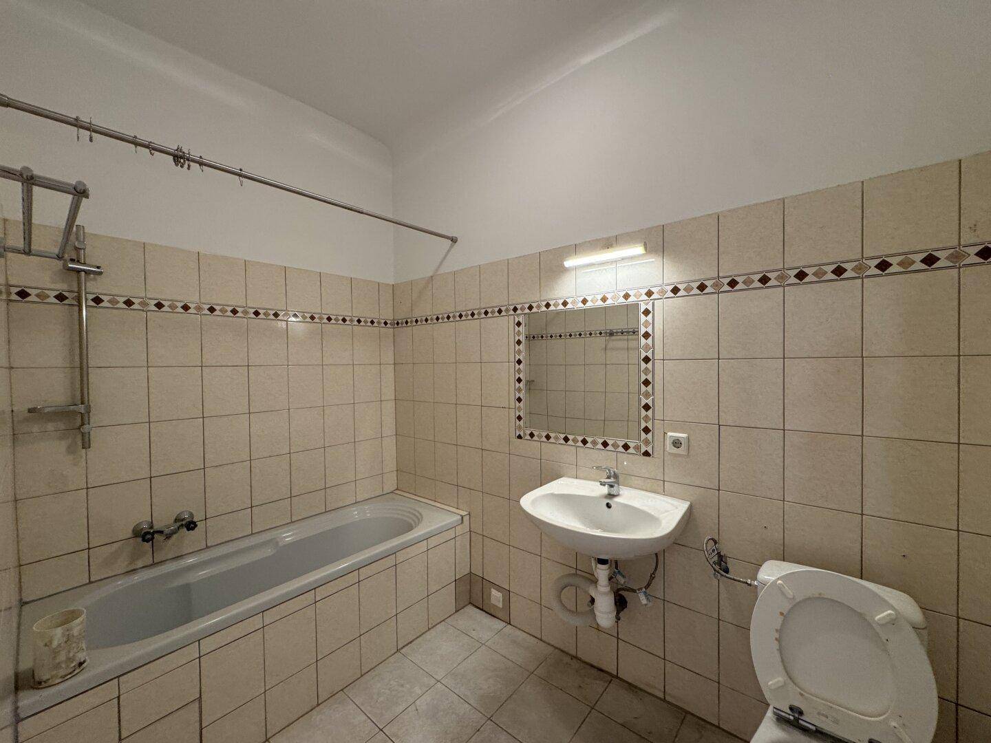 Badezimmer mit beigen Fliesen, Badewanne, Waschbecken und Toilette, im Stil der 80er Jahre.