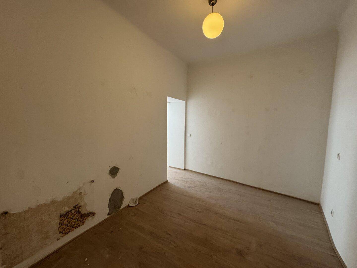 Leeres Zimmer mit Holzboden und beschädigten Wänden, renovierungsbedürftig.