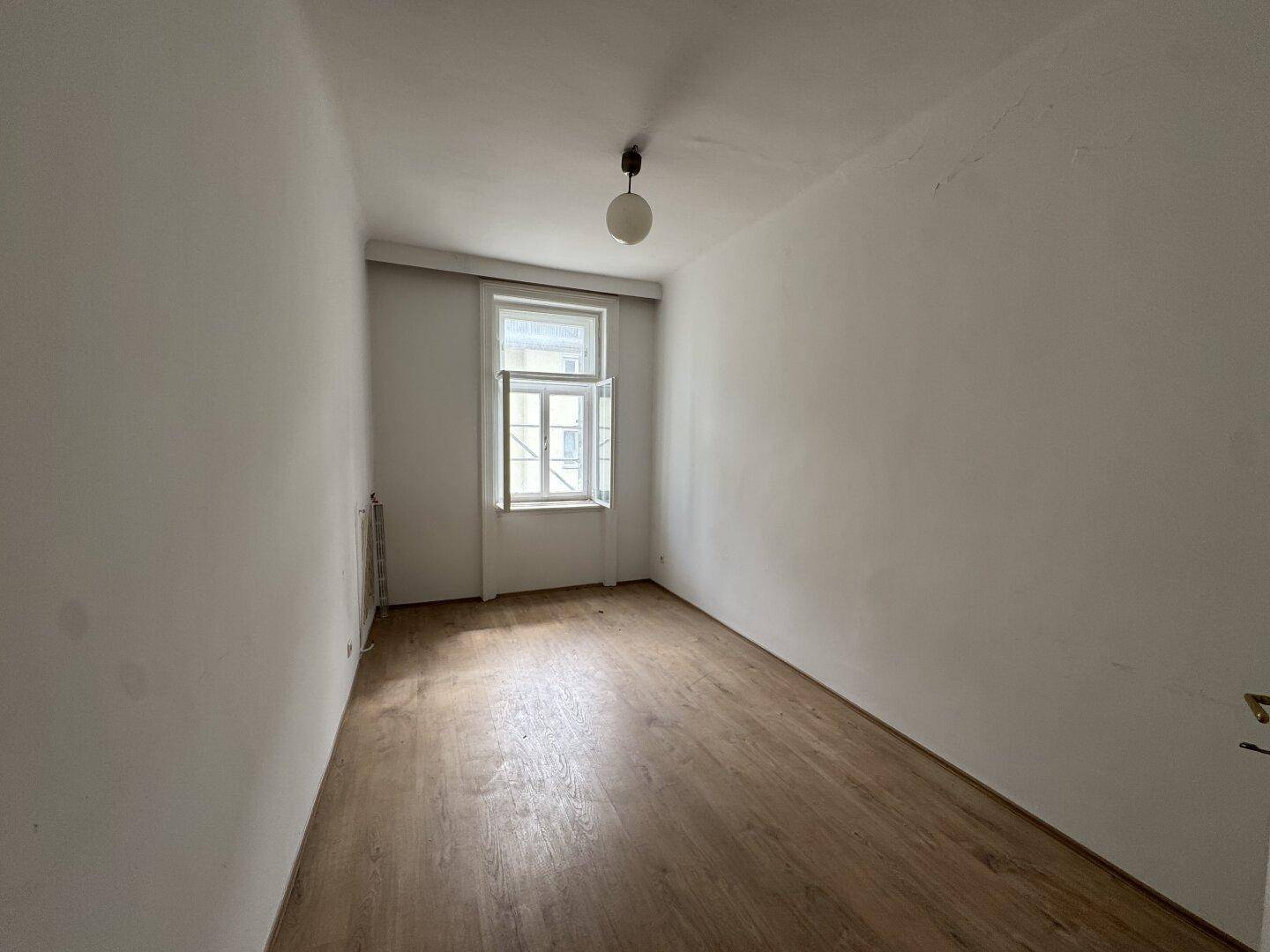 Leeres Zimmer mit Holzboden und einem Fenster, bereit zur individuellen Gestaltung.