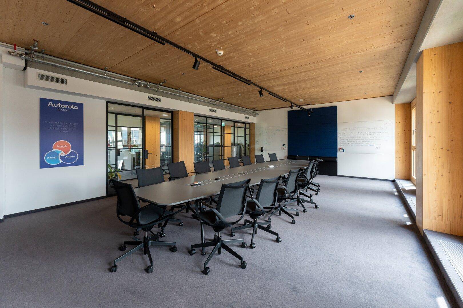 Konferenzraum mit Holzakzenten, Teppichboden, großem Tisch, blauer Akzentwand und Whiteboard.