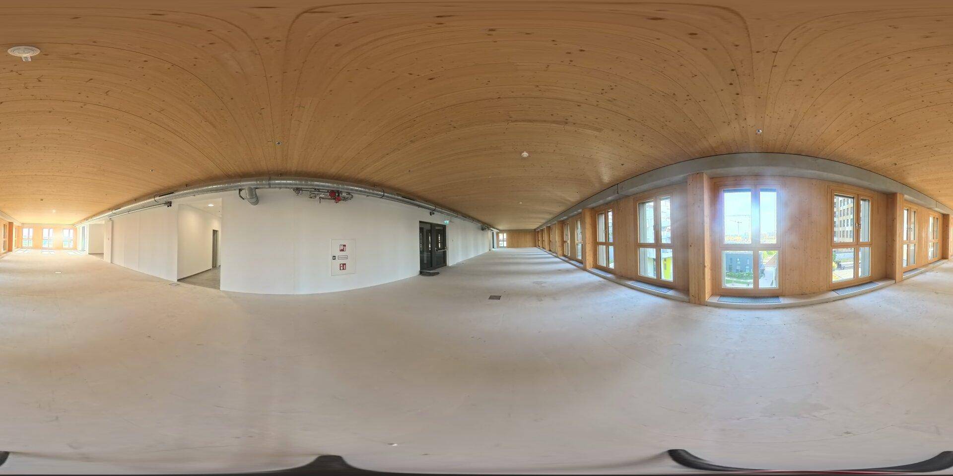 Panoramablick eines weitläufigen Gewerbebereichs mit gewölbter Holzdecke und vielen Fenstern.