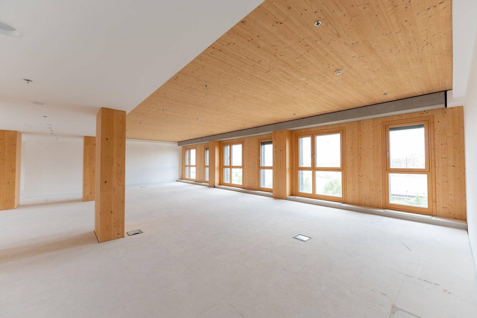 Heller und geräumiger Gewerberaum mit Holzelementen an Decke und Säulen sowie großen Fenstern.