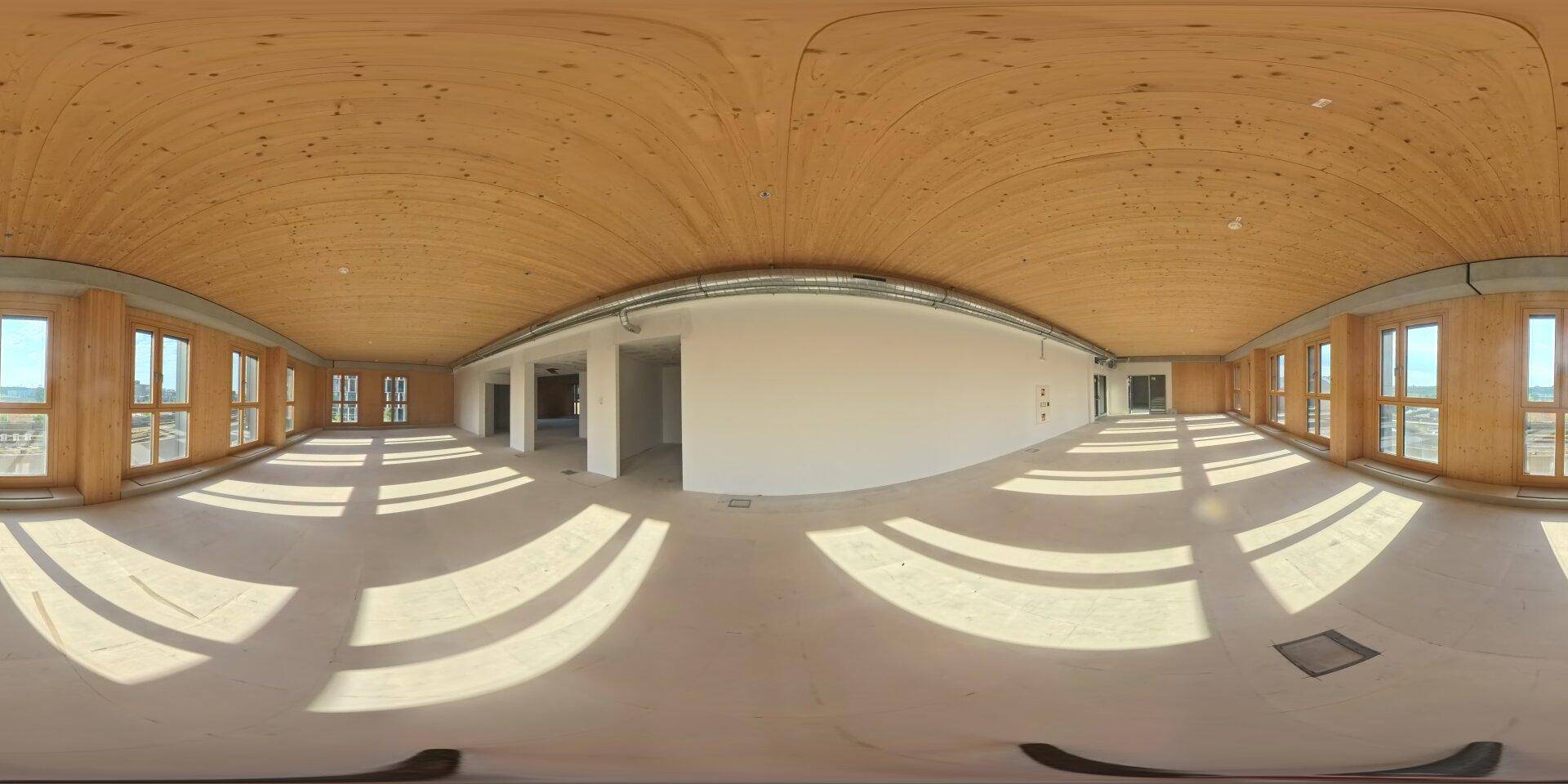 Weitläufiger, leerer Gewerberaum mit gewölbter Holzdecke, vielen Fenstern und Betonboden.