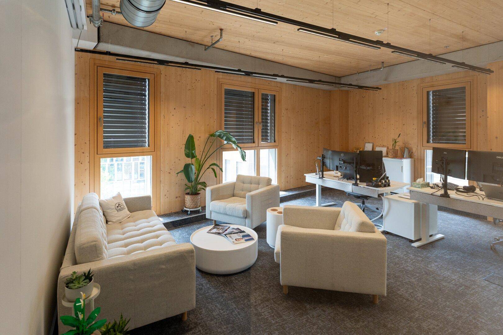 Modernes Büro mit Holzwänden und -decke, beigen Sitzmöbeln und Arbeitsplätzen mit Monitoren.