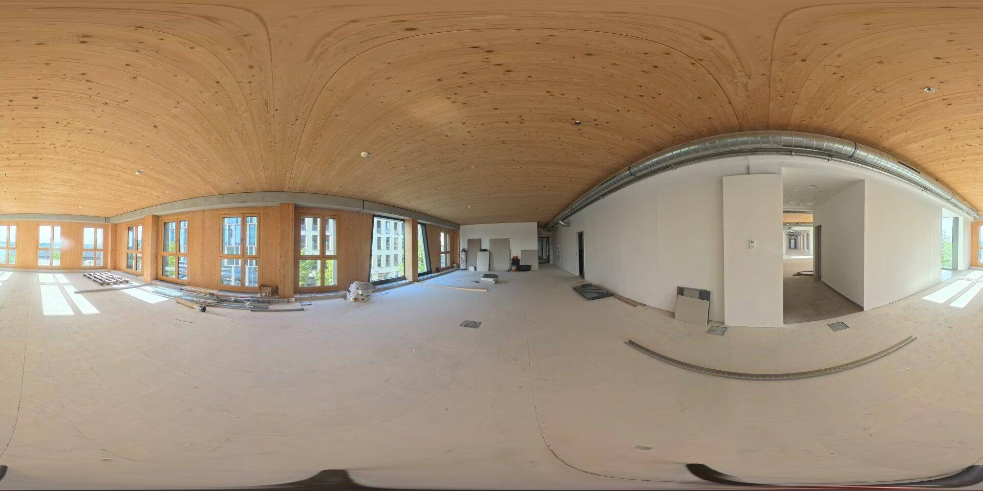 Großer, leerer Büroraum im Rohbau mit vielen Fenstern und einer beeindruckenden Holzdecke.