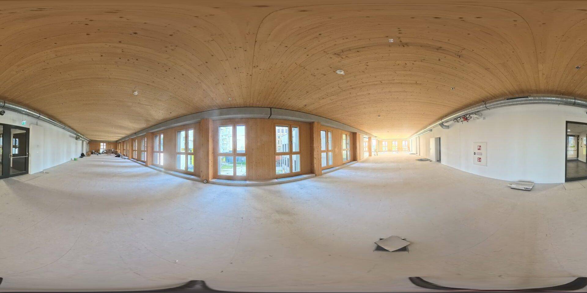 Großer, leerer Raum mit Holzbalkendecke und vielen Fenstern, bereit für den Ausbau als Bürofläche.