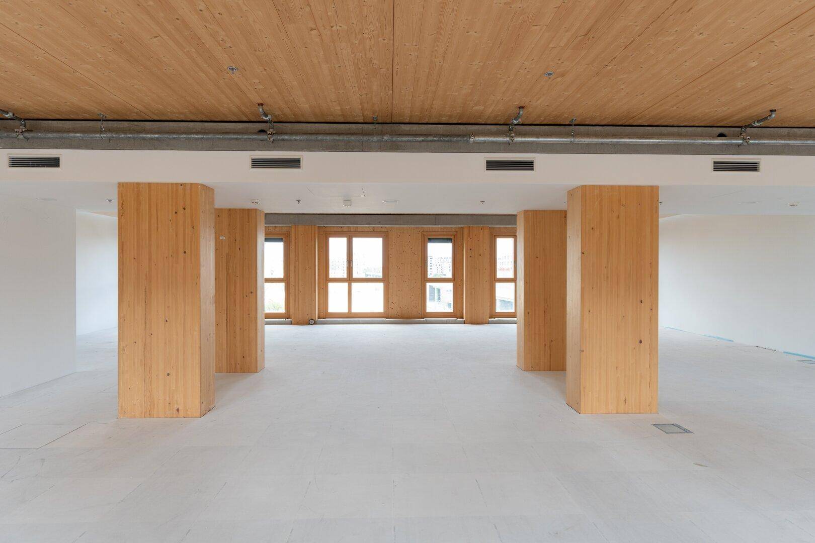 Heller, leerer Gewerberaum mit Holzstützen, Holzdecke und großen Fenstern, ideal für flexible Gestaltung.