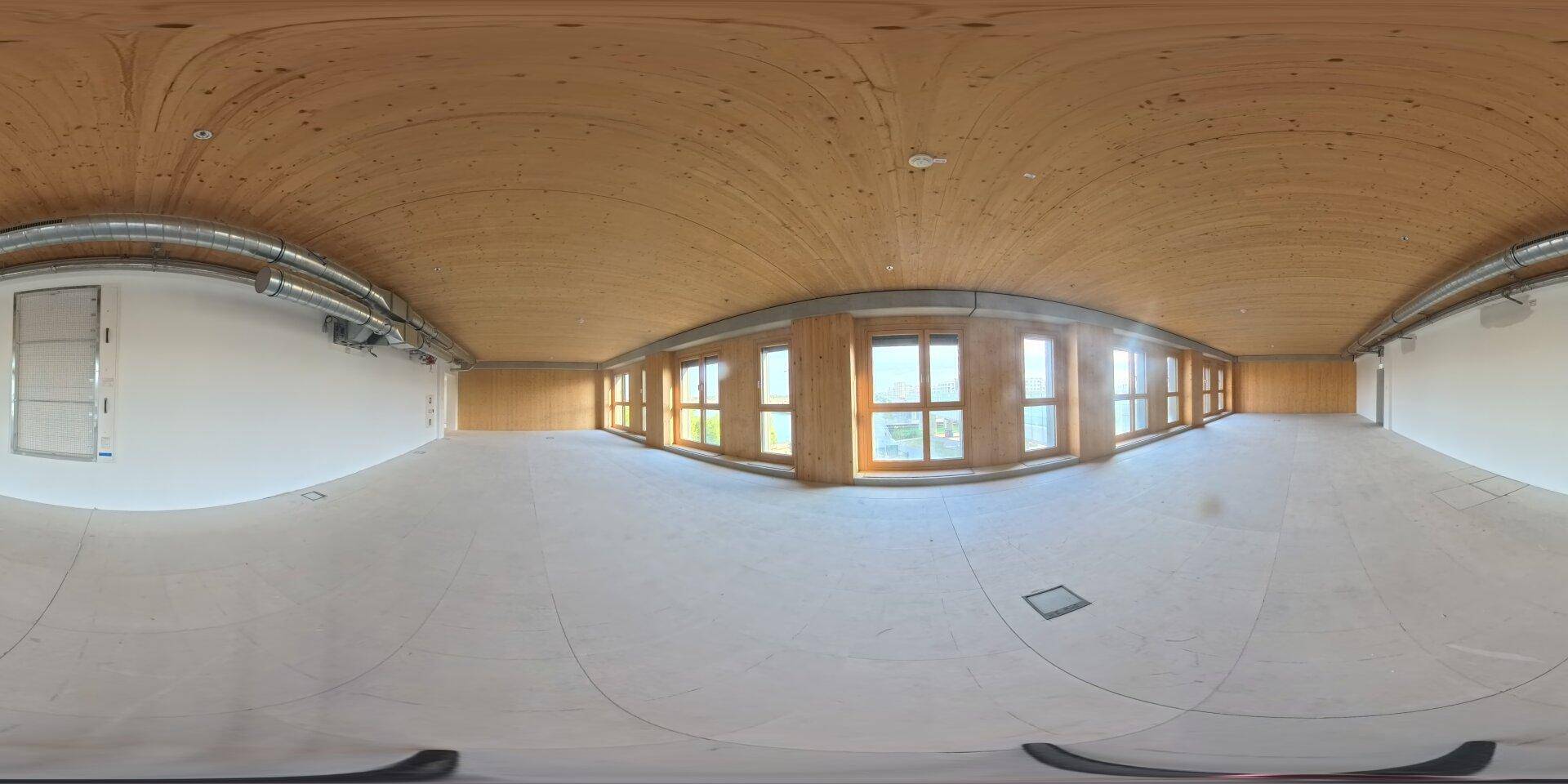 Leerer Gewerberaum mit Holzdecke, vielen Fenstern und sichtbaren Lüftungsrohren, bereit für den Ausbau.