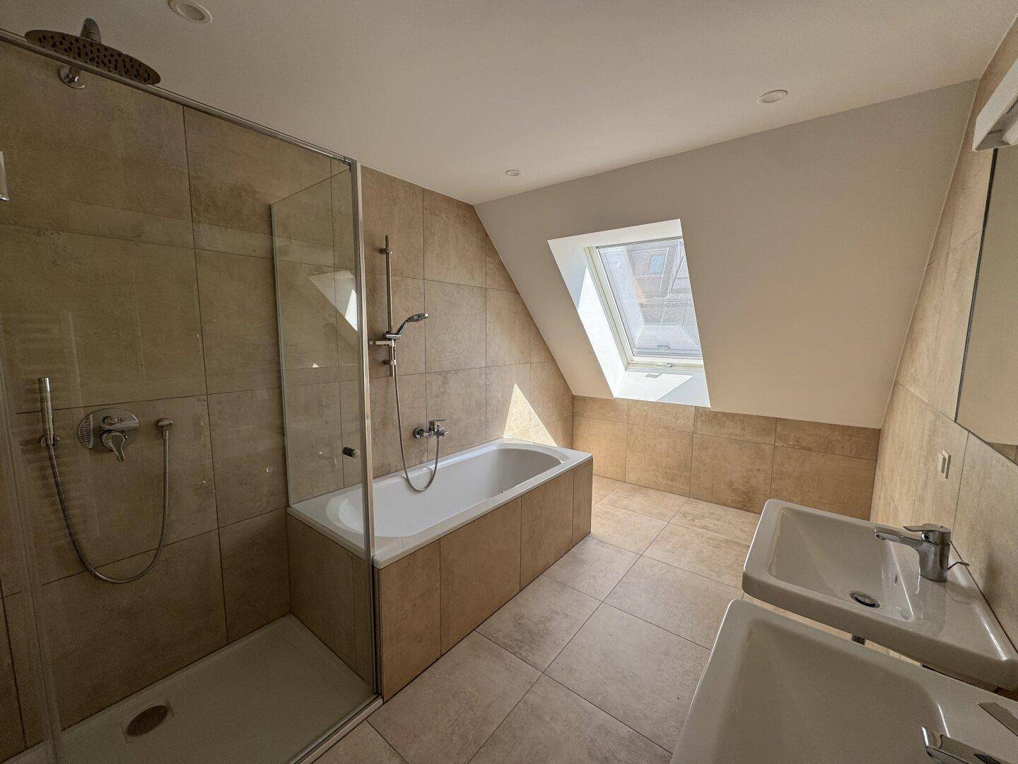 Modernes Badezimmer mit beigen Fliesen, Badewanne, begehbarer Dusche, Doppelwaschbecken und Dachfenster.