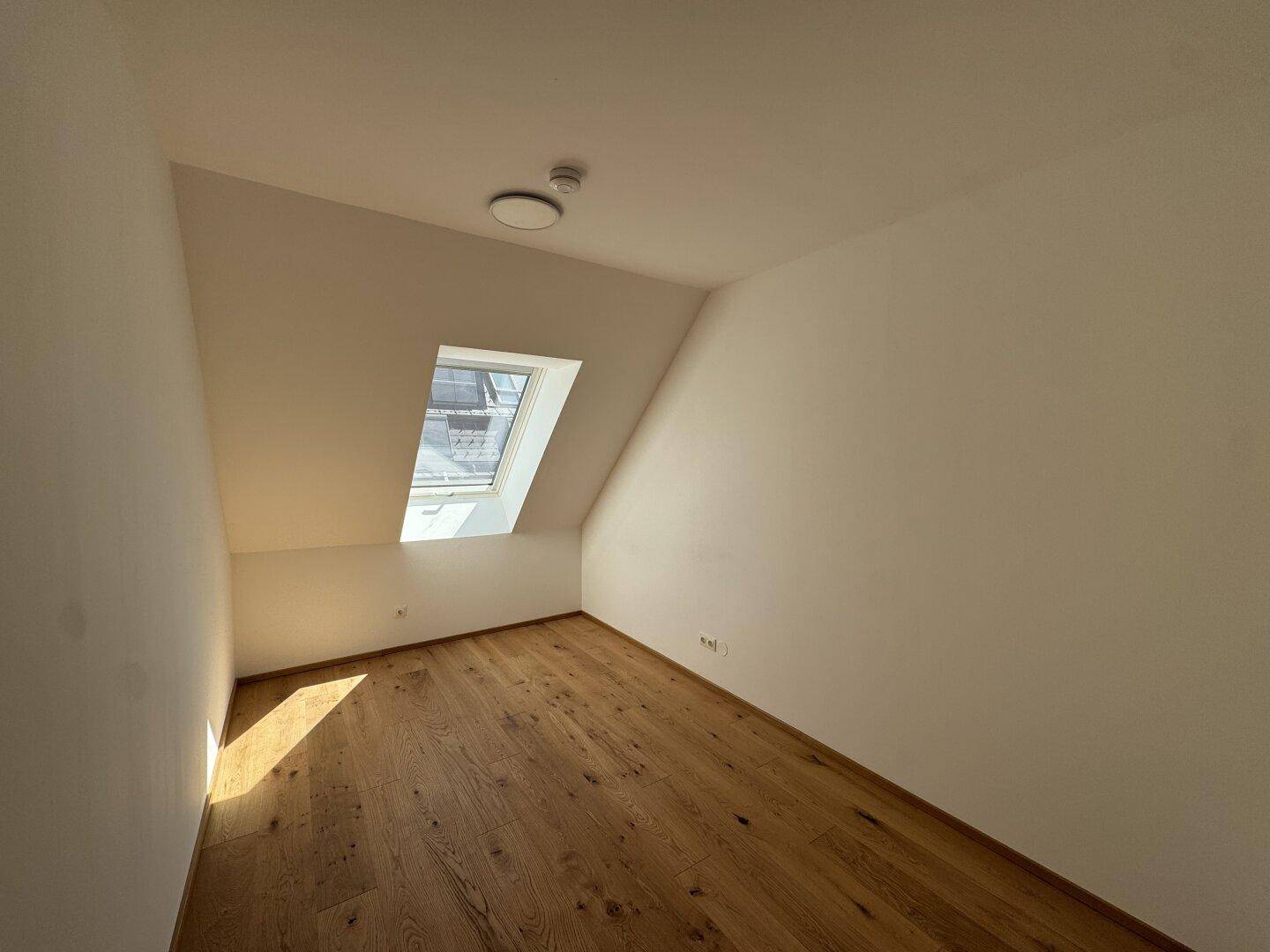 Helles Schlafzimmer mit Holzboden, Dachschräge und einem Dachfenster für natürliches Licht.