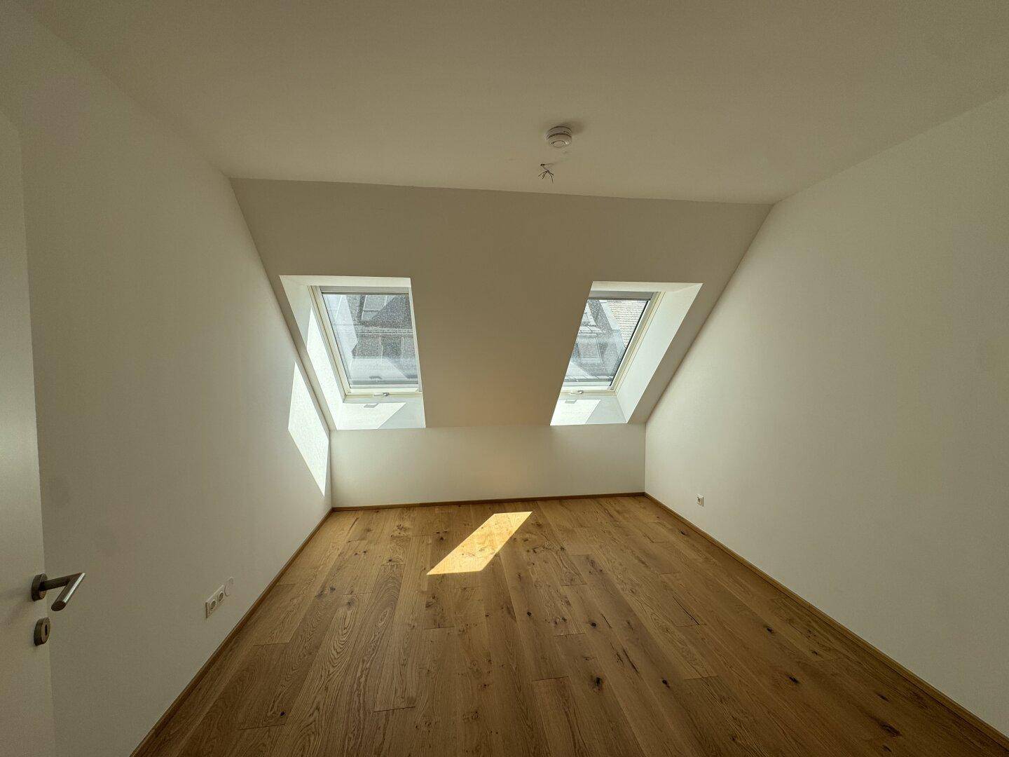 Geräumiges Schlafzimmer mit Holzboden, Dachschrägen und zwei hellen Dachfenstern.