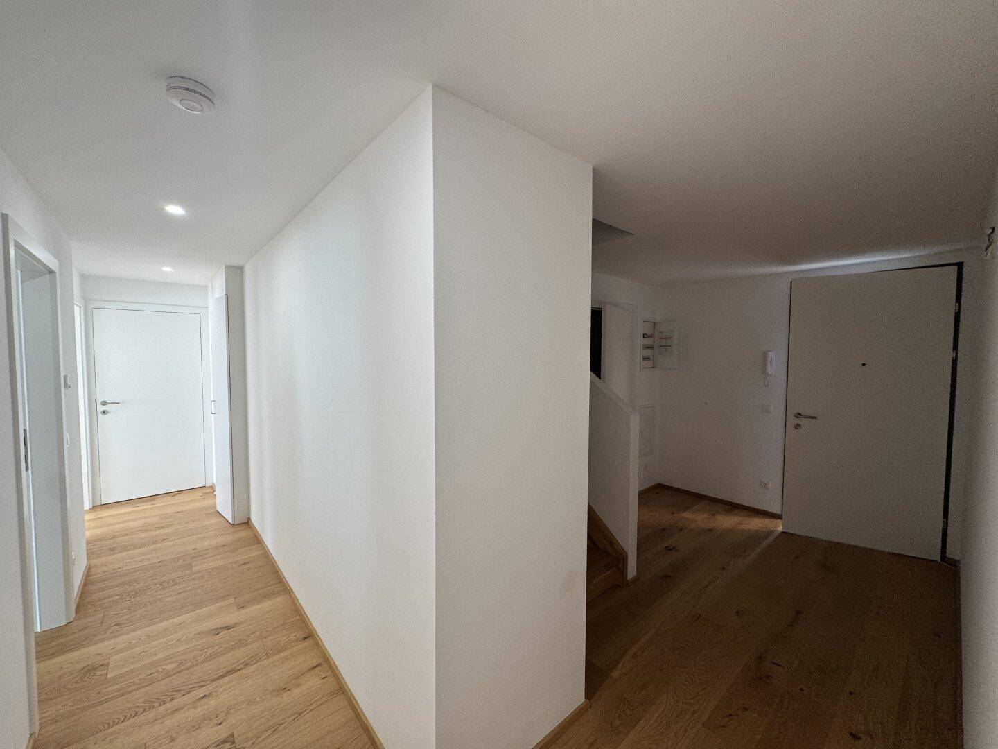Heller Flur mit Holzboden und weißen Wänden, der zu den verschiedenen Räumen der Wohnung führt.