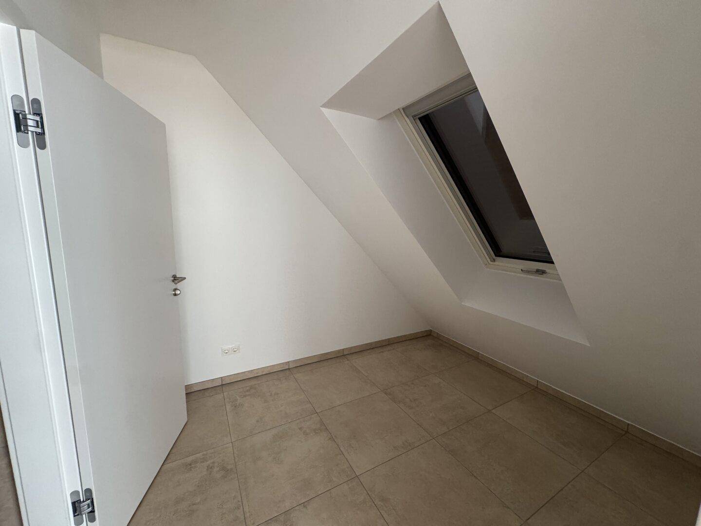 Kleiner, heller Raum mit Fliesenboden, Dachschräge und einem Dachfenster für Tageslicht.