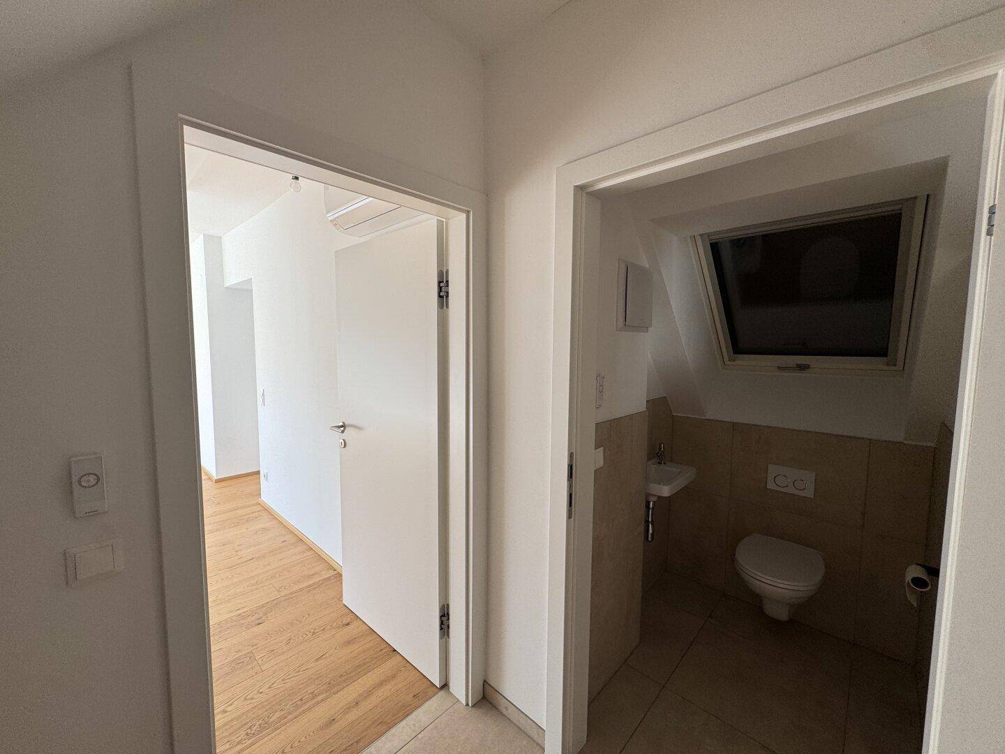 Modernes Gäste-WC mit Fliesenboden, Toilette, kleinem Waschbecken und Dachfenster.
