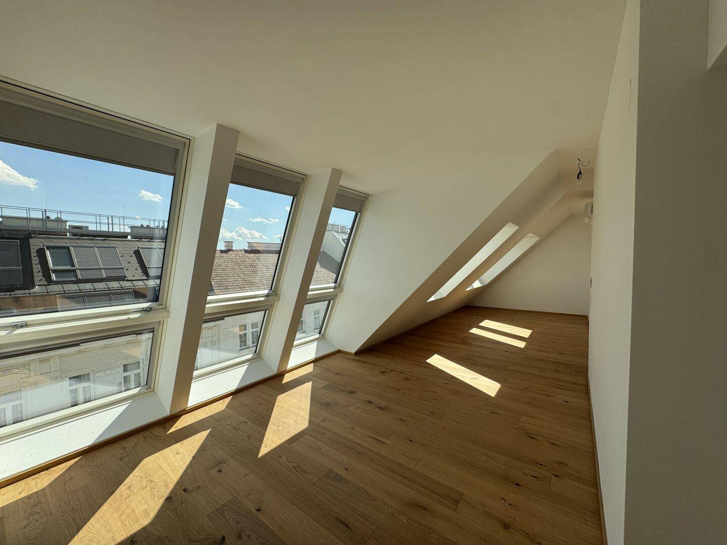 Heller Raum mit Holzboden, Dachschrägen und großen Fenstern mit weitem Blick über die Dächer.