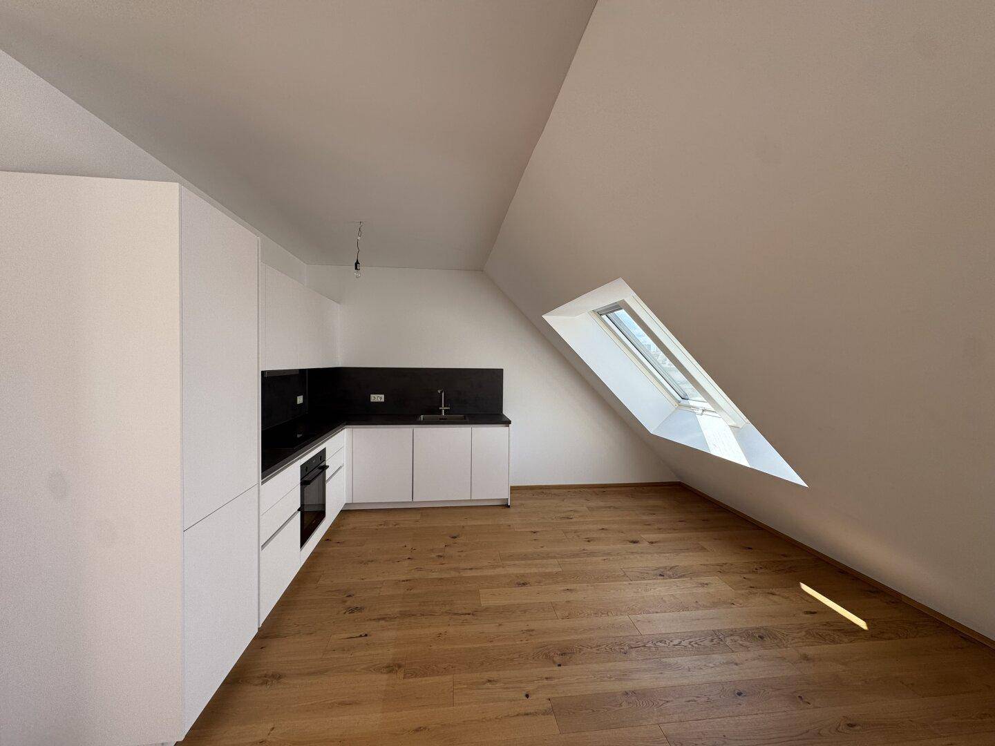 Moderne Küchenzeile mit weißen Schränken, dunkler Arbeitsplatte, integriertem Ofen und Dachfenster.