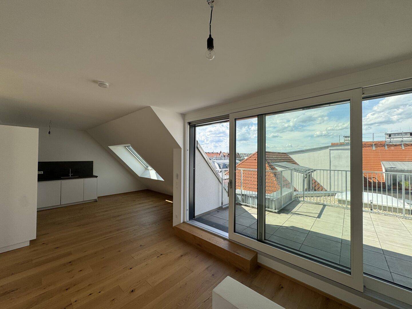 Heller Wohnbereich mit Holzboden, Dachschrägen und großem Schiebefenster zur sonnigen Dachterrasse.